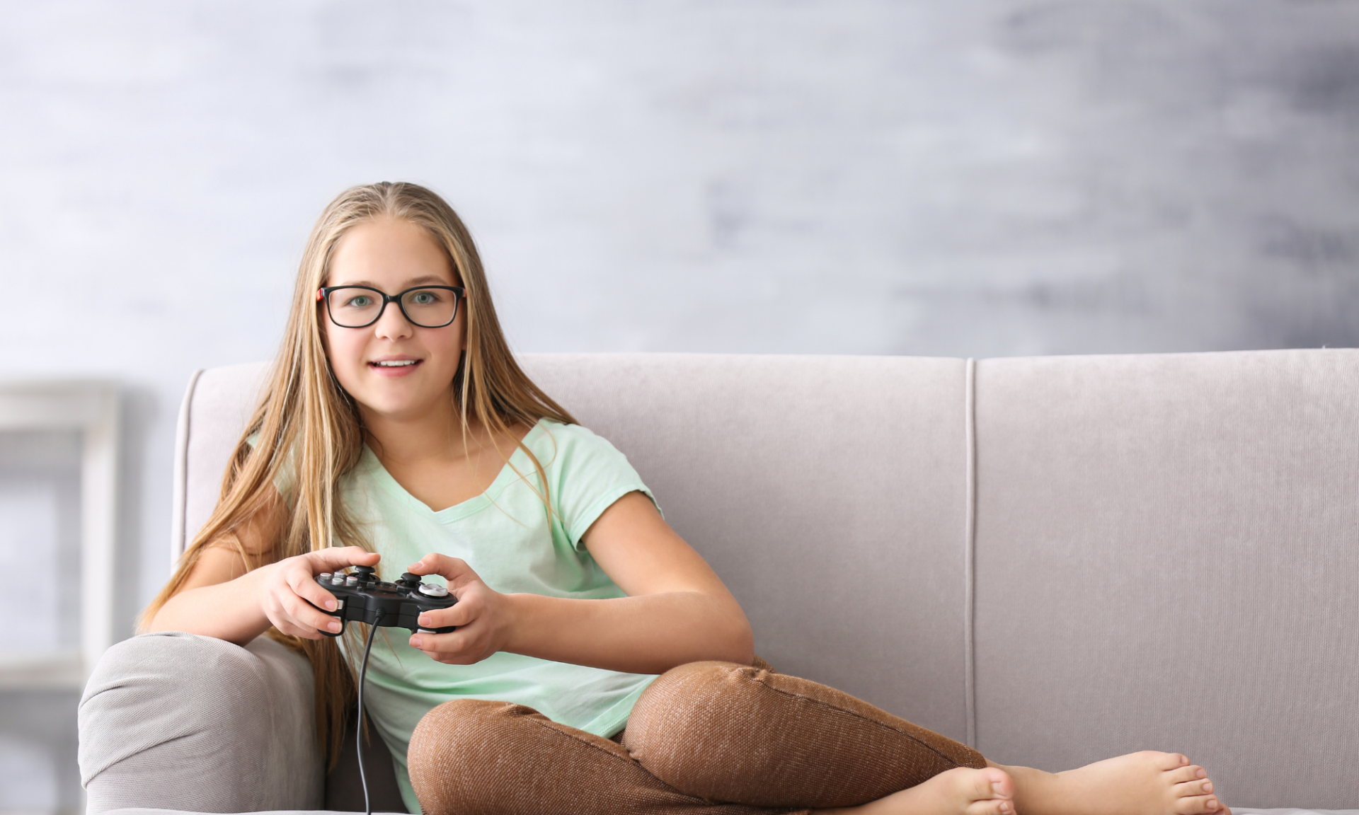 A girl curls up on a couch holding a video game controller.